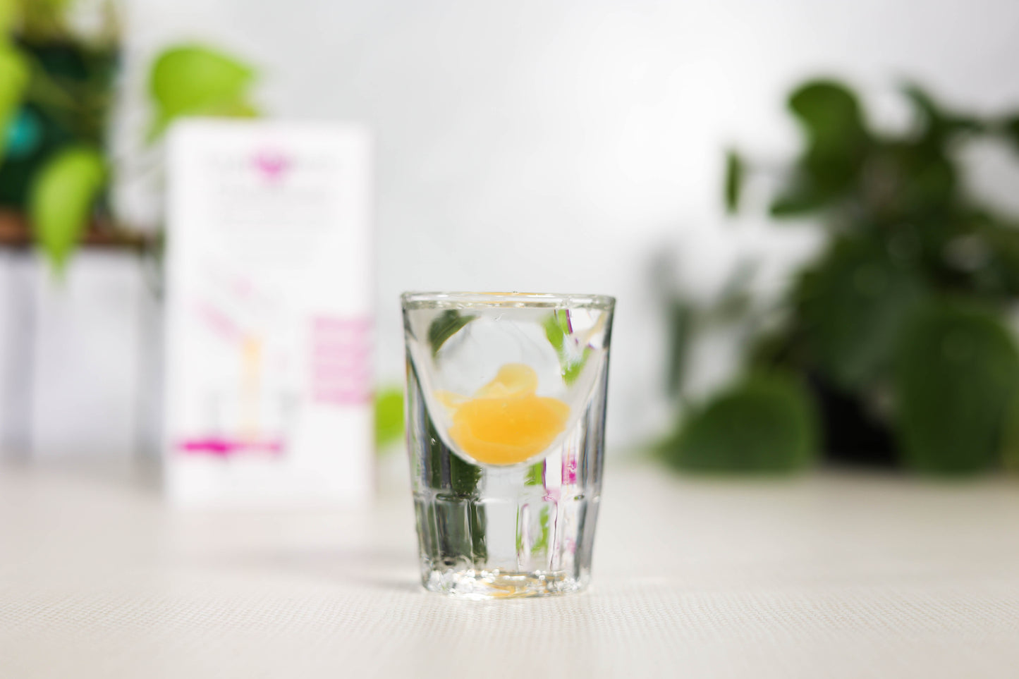 Clear glass with Glutathione liquid supplement on a white surface with blurred greenery in the background